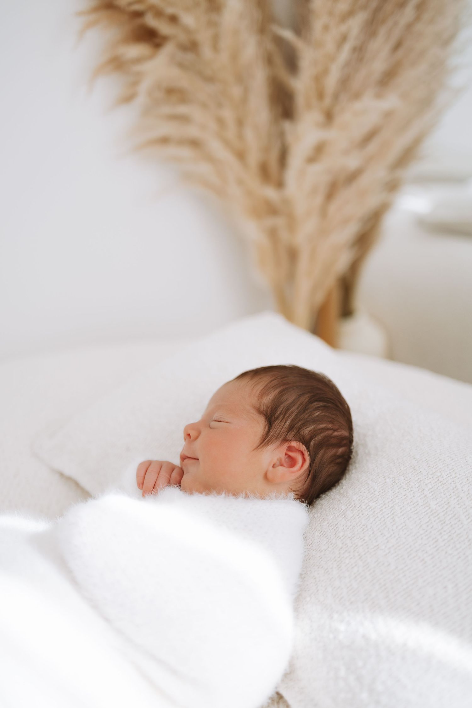 Sleeping newborn baby wrapped in white blanket rests peacefully on soft white bedding.