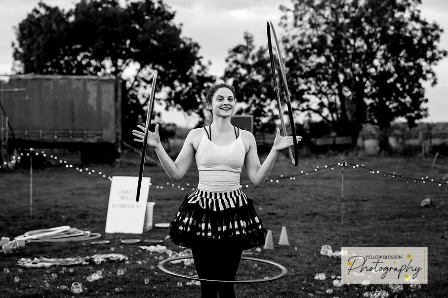Black and white image showing people playing with bubble balls and hula hoops in a grassy field.