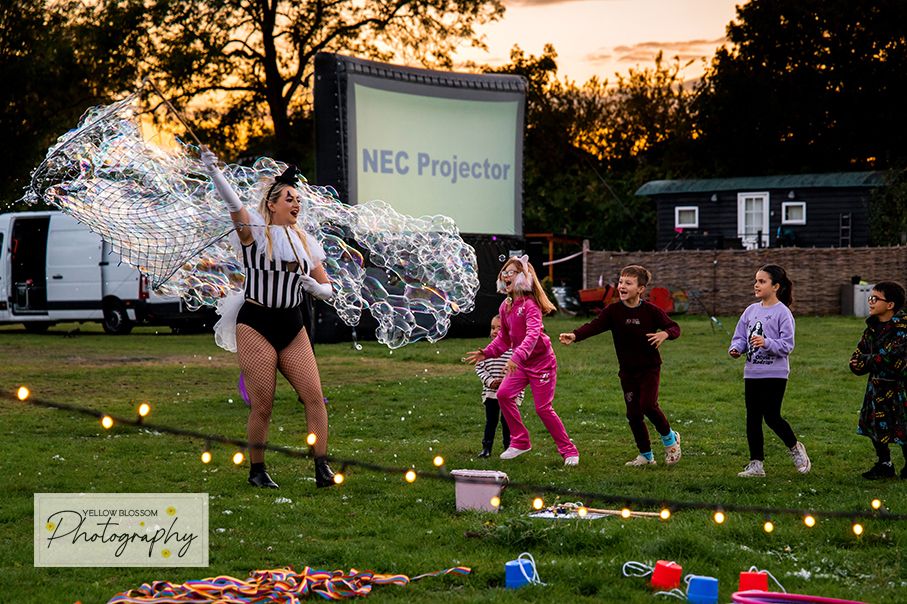 People gathered on a lawn at sunset with glowing lights scattered across the grass during an outdoor event.
