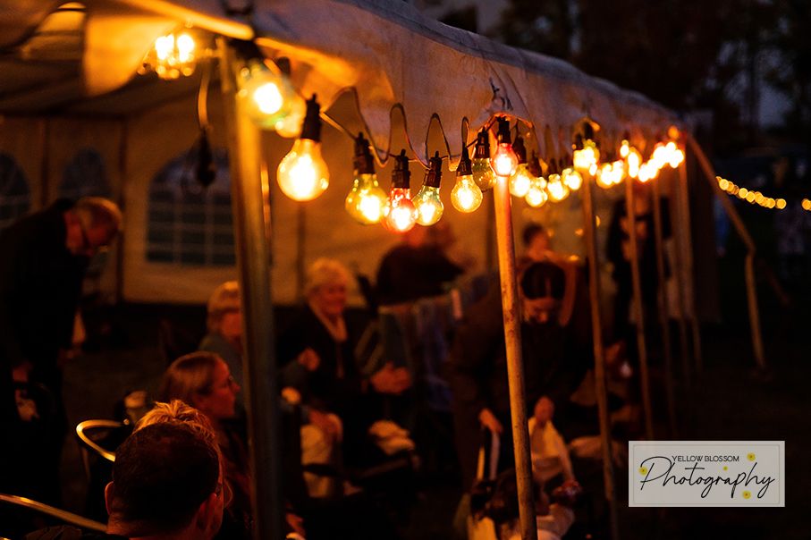 String lights illuminate a rustic outdoor dining area at dusk creating a warm and romantic ambiance.