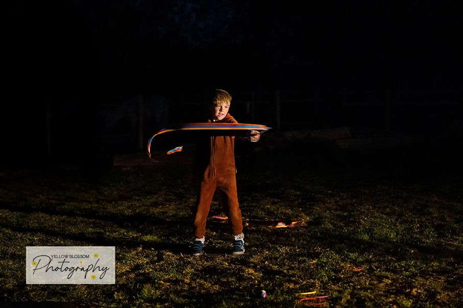 A silhouetted figure performs light painting with sparklers at night creating glowing trails against a dark background.