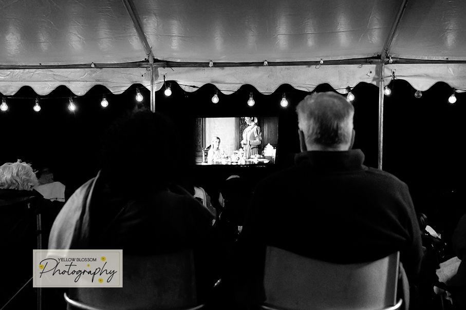 Wedding guests enjoy a candlelit reception dinner under a white tent with string lights overhead.