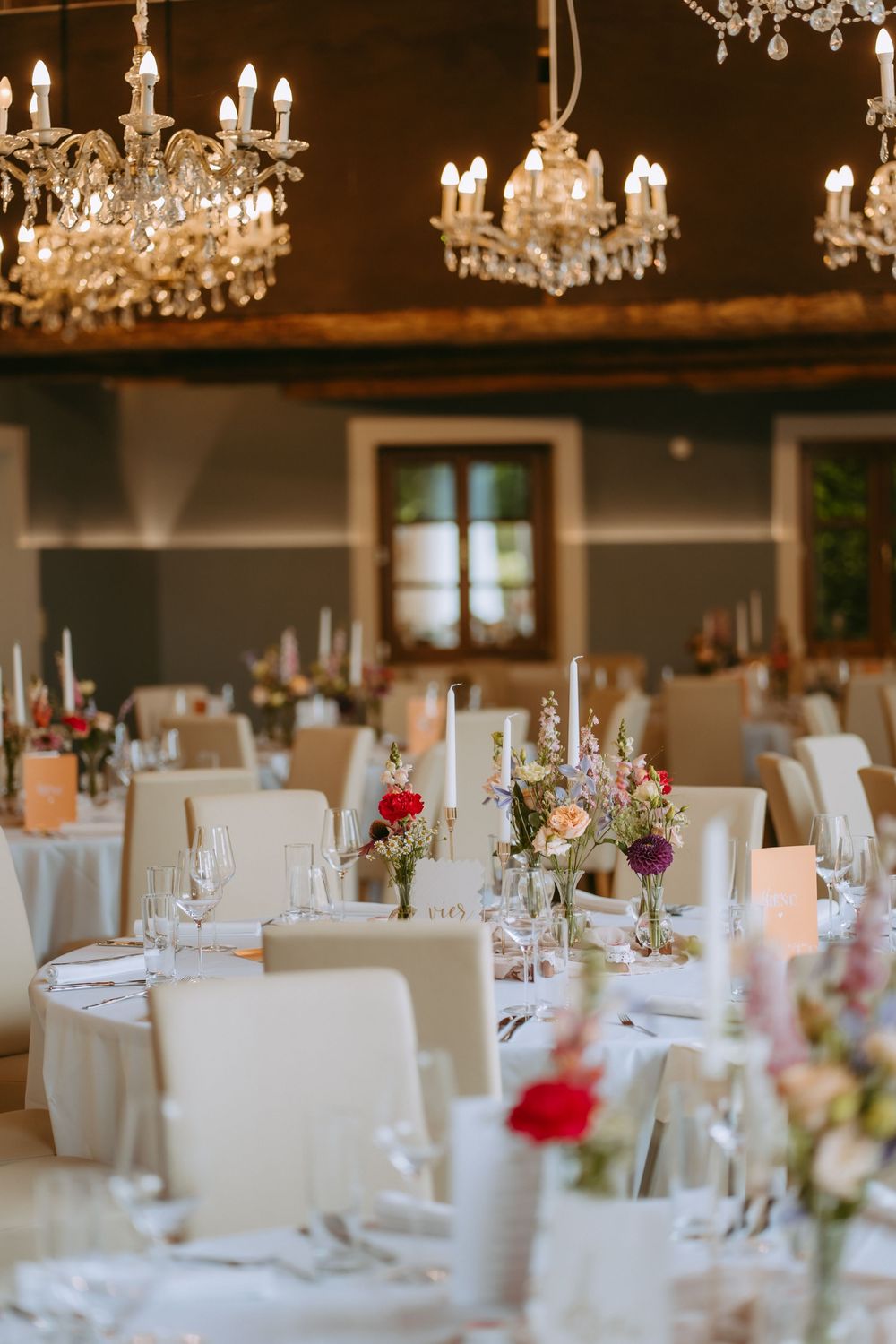 Elegant wedding reception tables set with crystal chandeliers, white linens, and floral centerpieces.