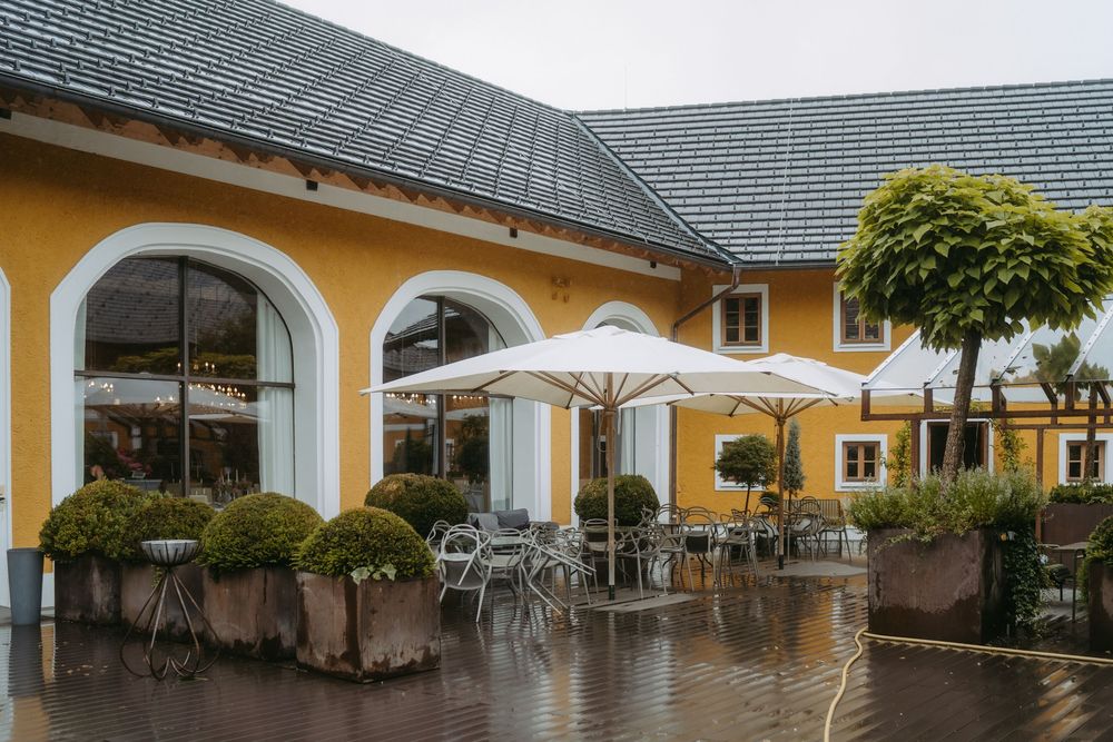 Yellow building exterior with outdoor patio seating and white umbrellas on a rainy day.