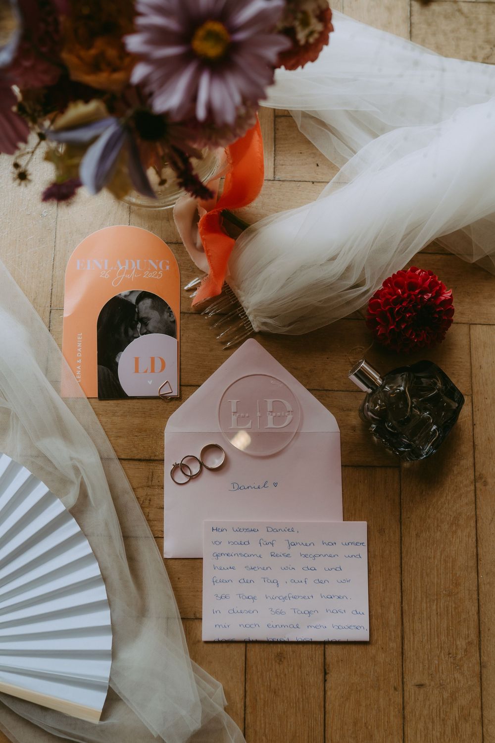 Wedding invitation details with rings, tulle, and floral decorations on wooden surface.