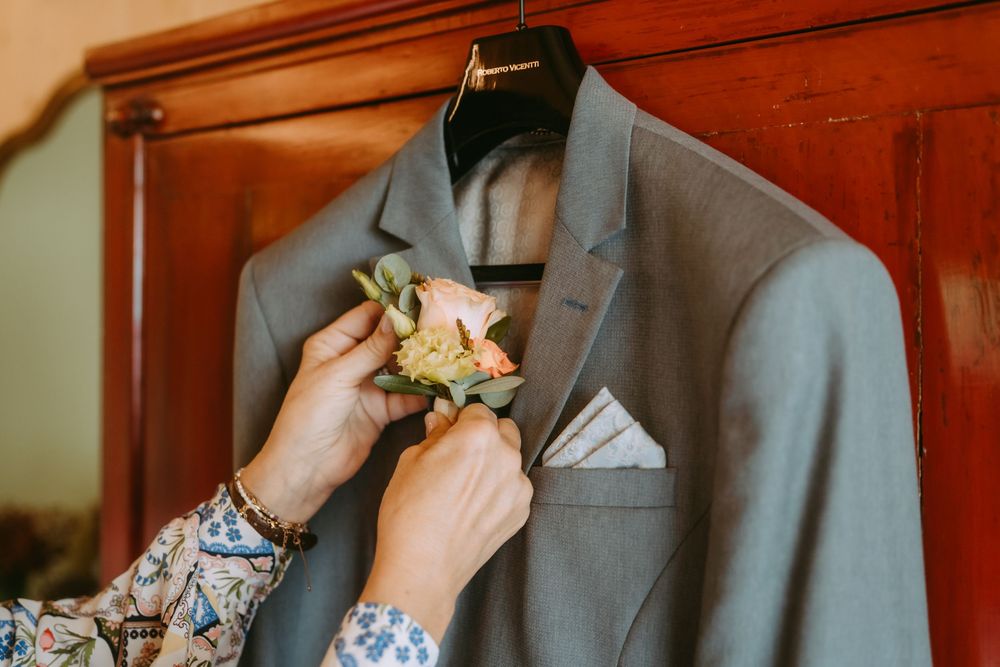 Hands pinning boutonniere to gray suit jacket lapel.