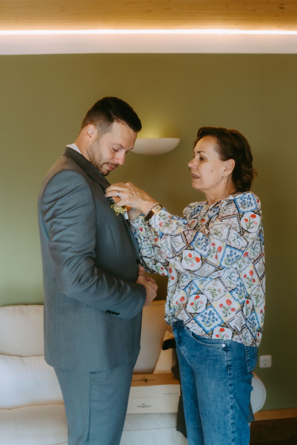 Getting ready scene with boutonniere being pinned to gray suit.