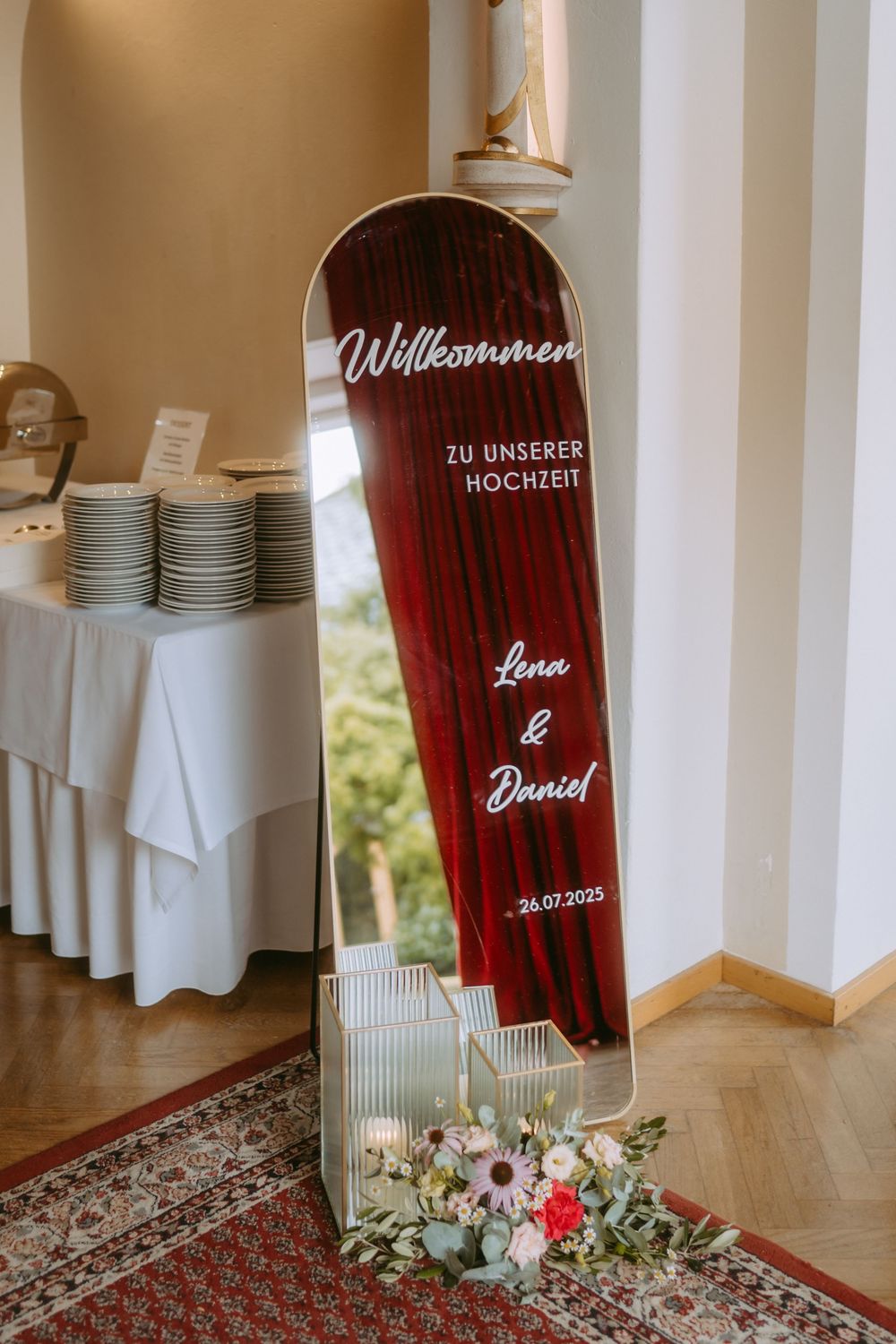 Wedding reception welcome sign and decor with red curtains and elegant table settings.