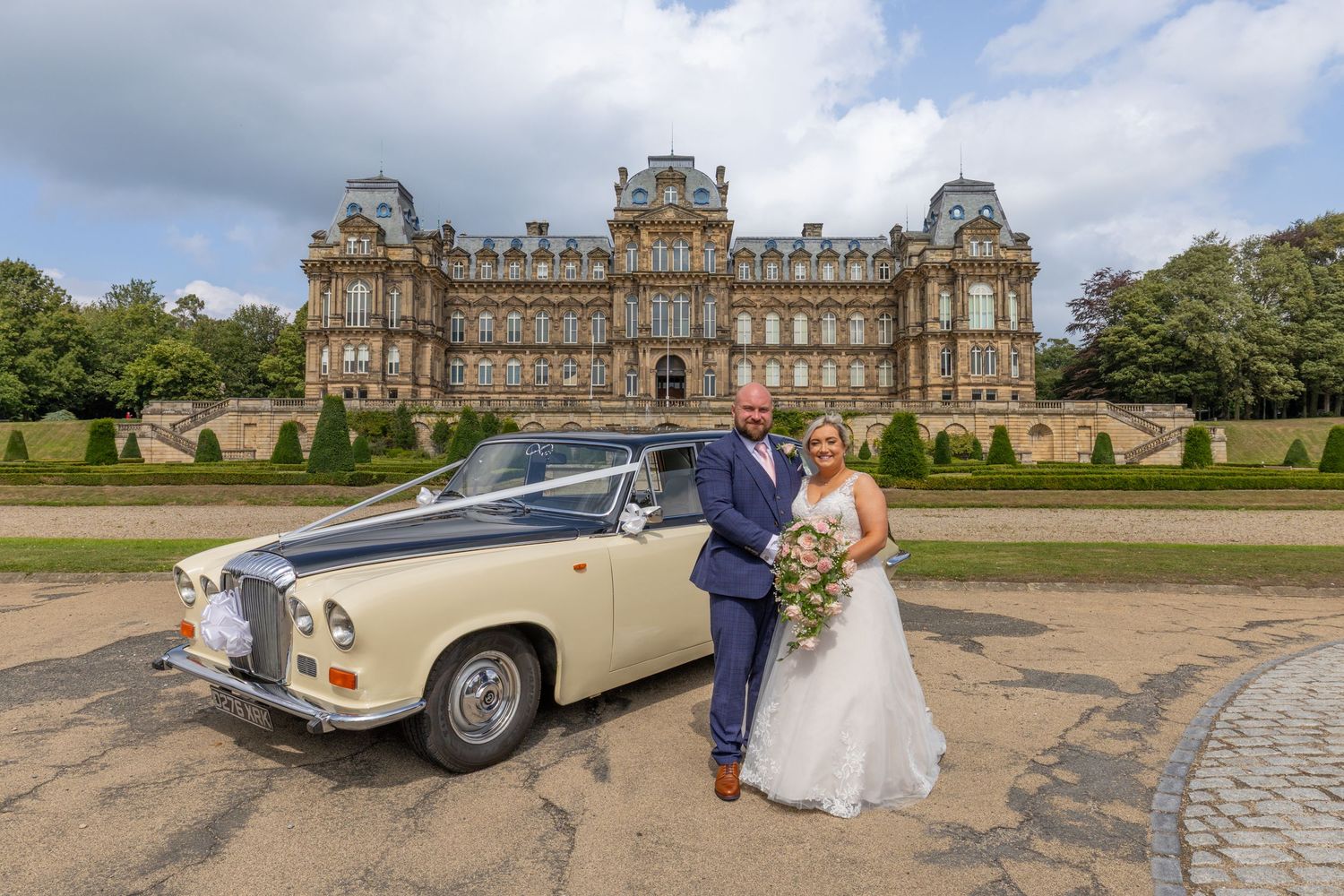 Classic vintage Rolls Royce wedding car parked in front of a grand historic mansion estate.