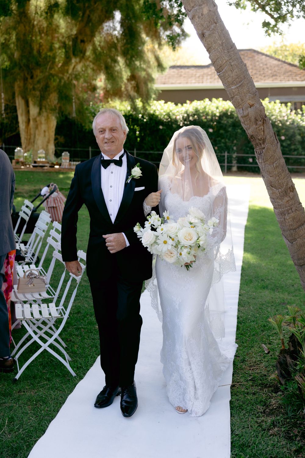 A series of outdoor wedding ceremony photos showing a couple walking together under trees with white chairs in the background.