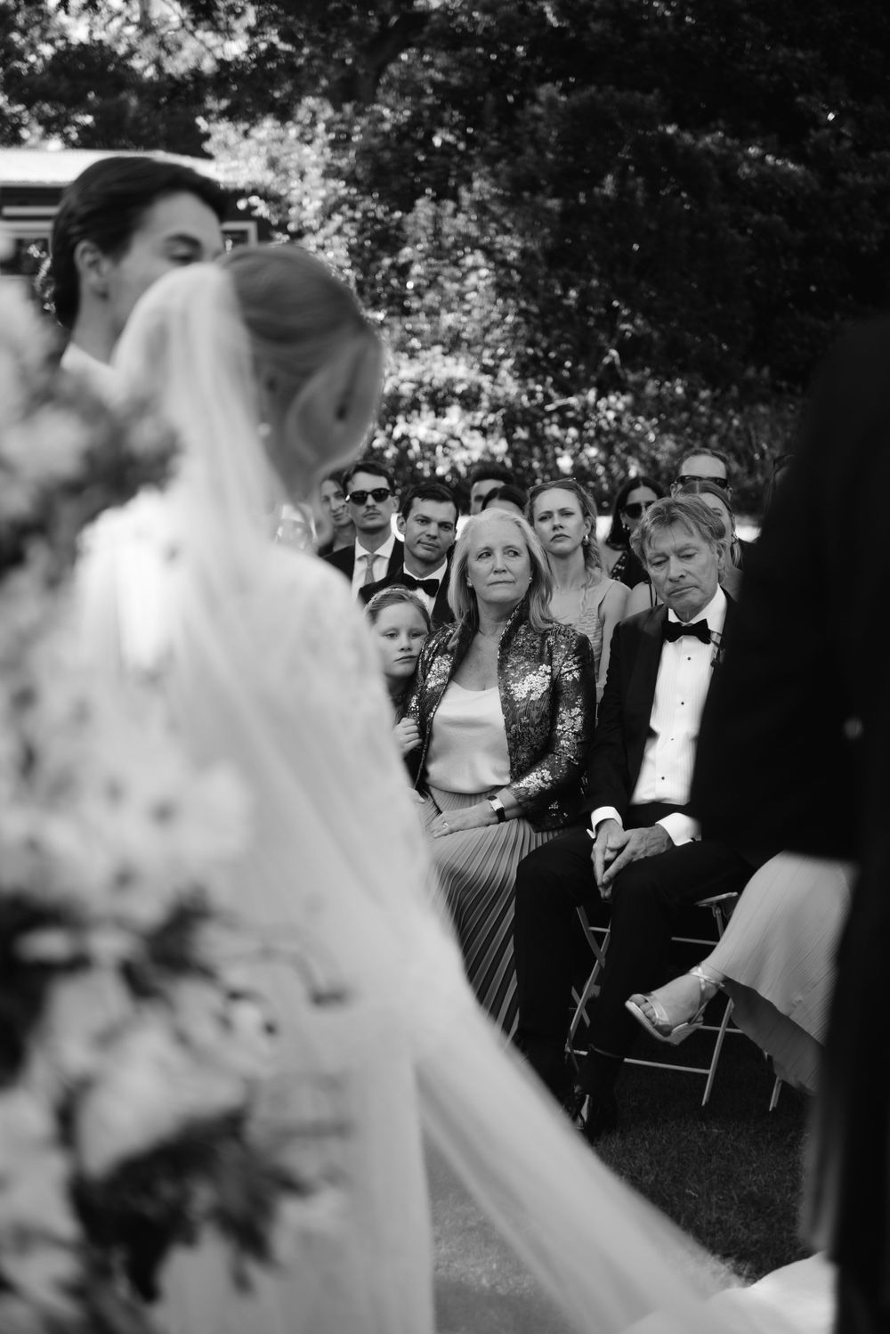 Black and white wedding photos showing guests watching a ceremony with white chairs arranged outdoors.