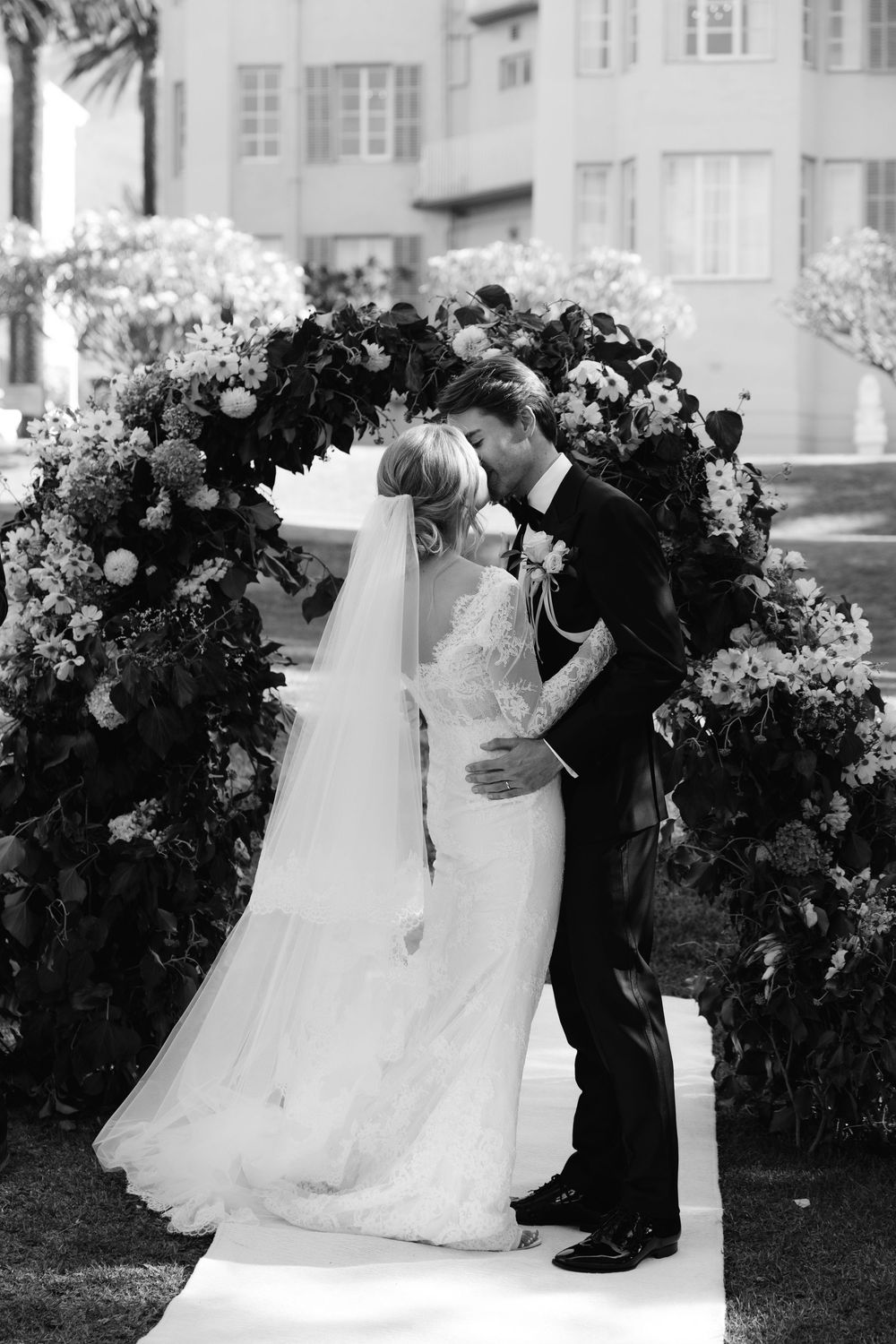 A romantic black and white wedding photo sequence showing a couple dancing together in front of floral arrangements.