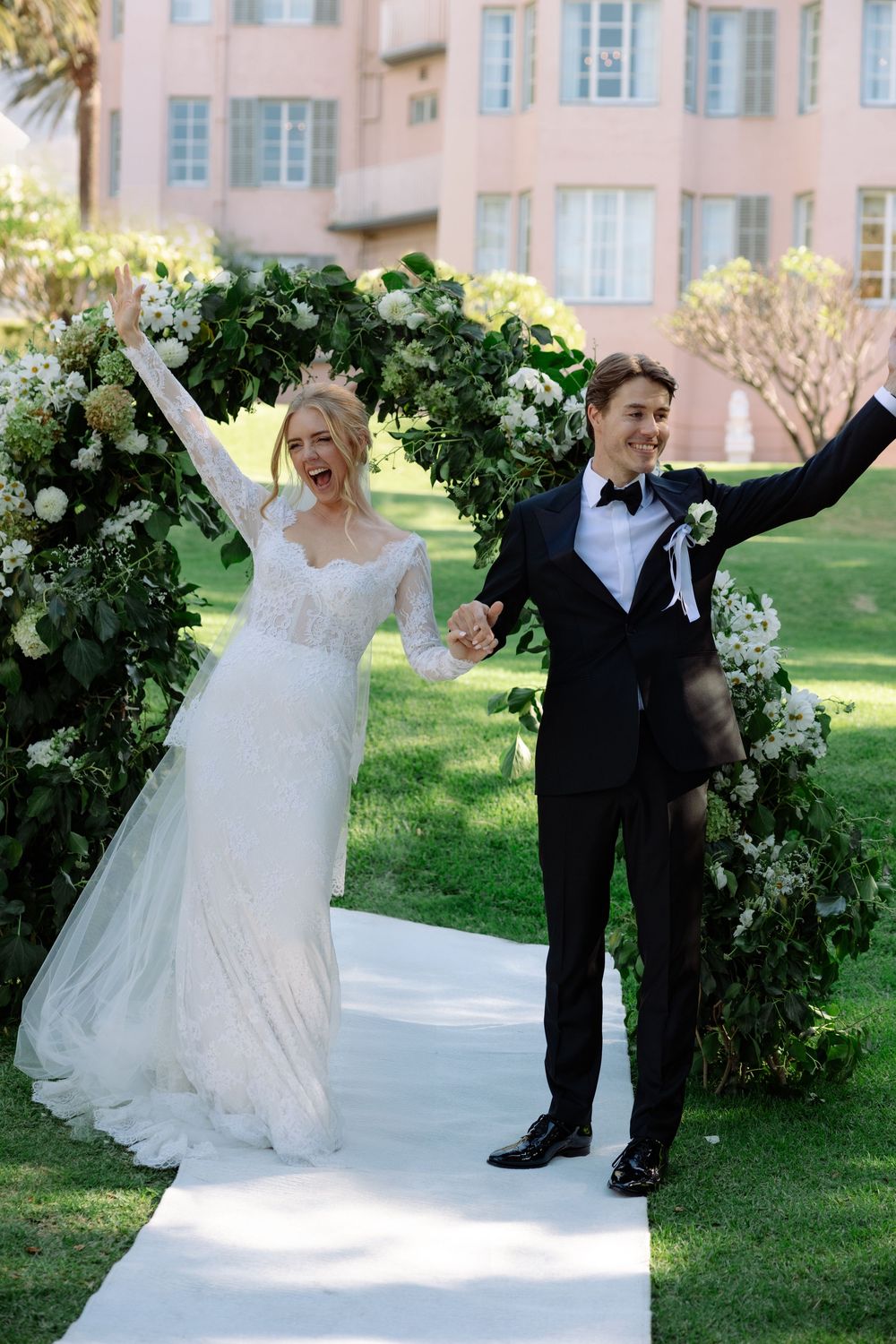 A joyful wedding celebration with dancing and laughter in front of a lush garden arch at an elegant venue.