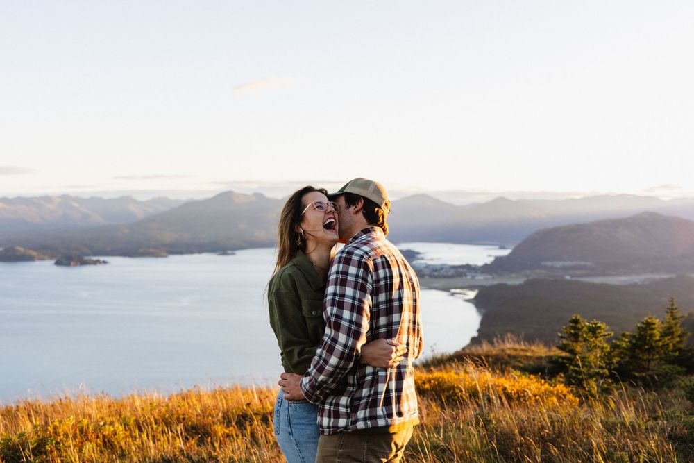 Two people share a romantic moment at sunset overlooking a scenic mountain vista and lake landscape.