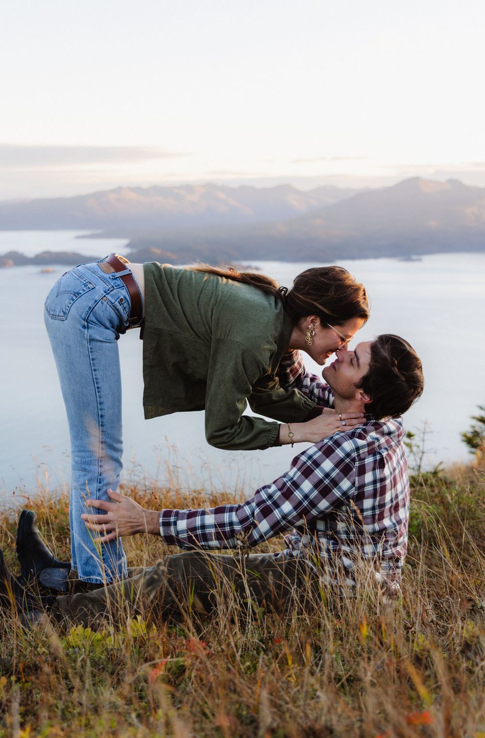 A romantic couple shares intimate moments in a scenic mountain meadow at sunset.