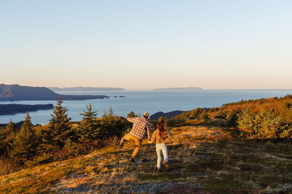 Panoramic coastal mountain landscape at sunset with golden light illuminating rocky terrain and evergreen trees.