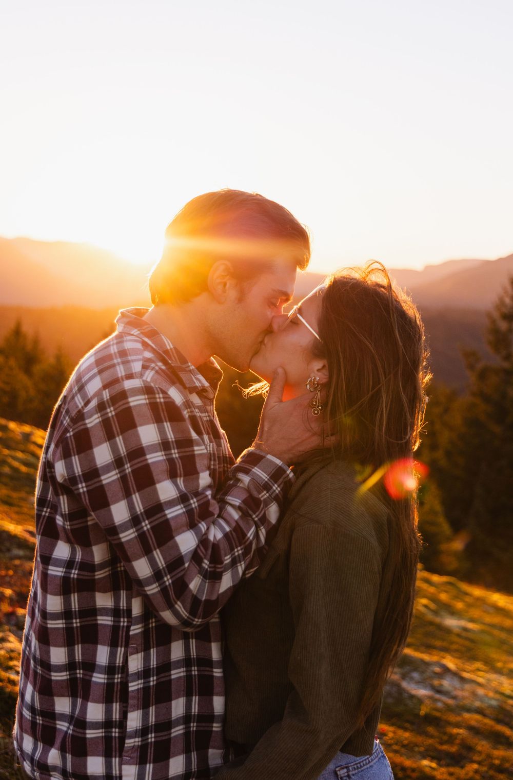 Couple sharing an intimate moment at sunset with golden light streaming through the trees.