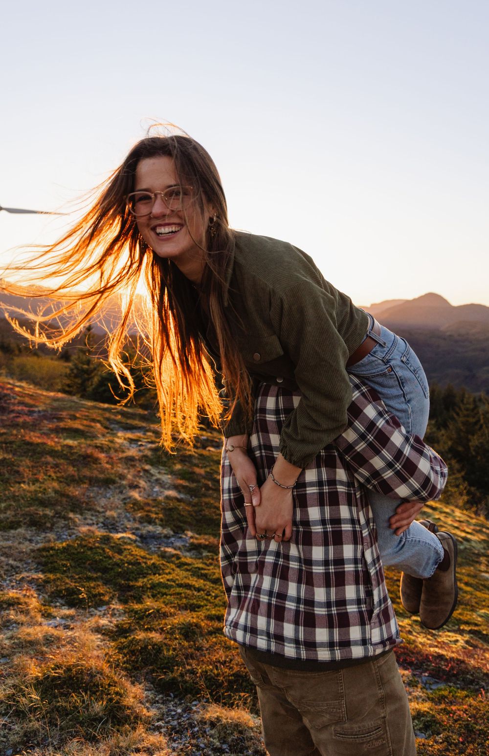 A person with flowing hair stands on a mountain slope at golden hour, creating a playful outdoor portrait series.