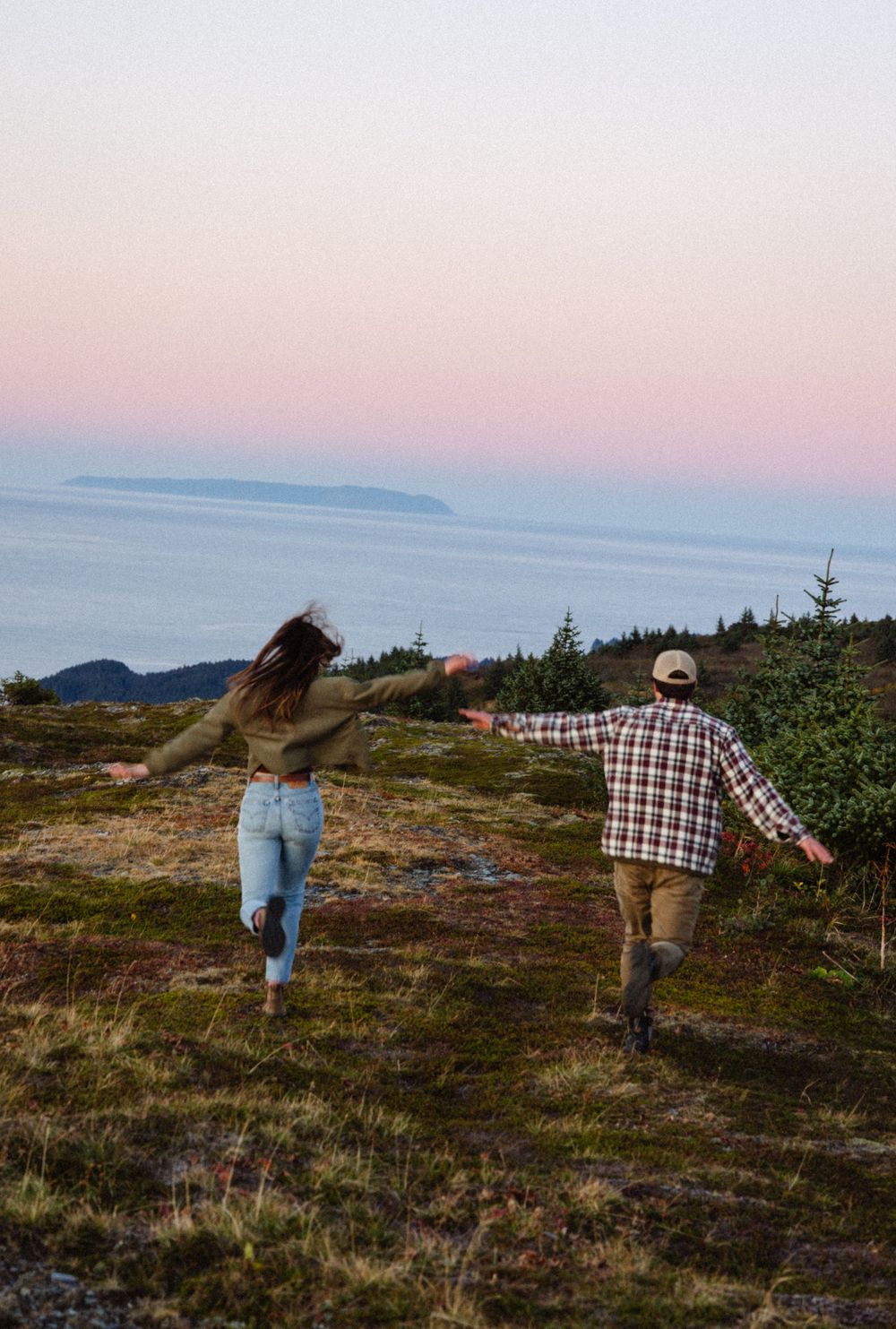 Two people walk hand in hand across a scenic coastal hilltop during golden hour with ocean views in the background.