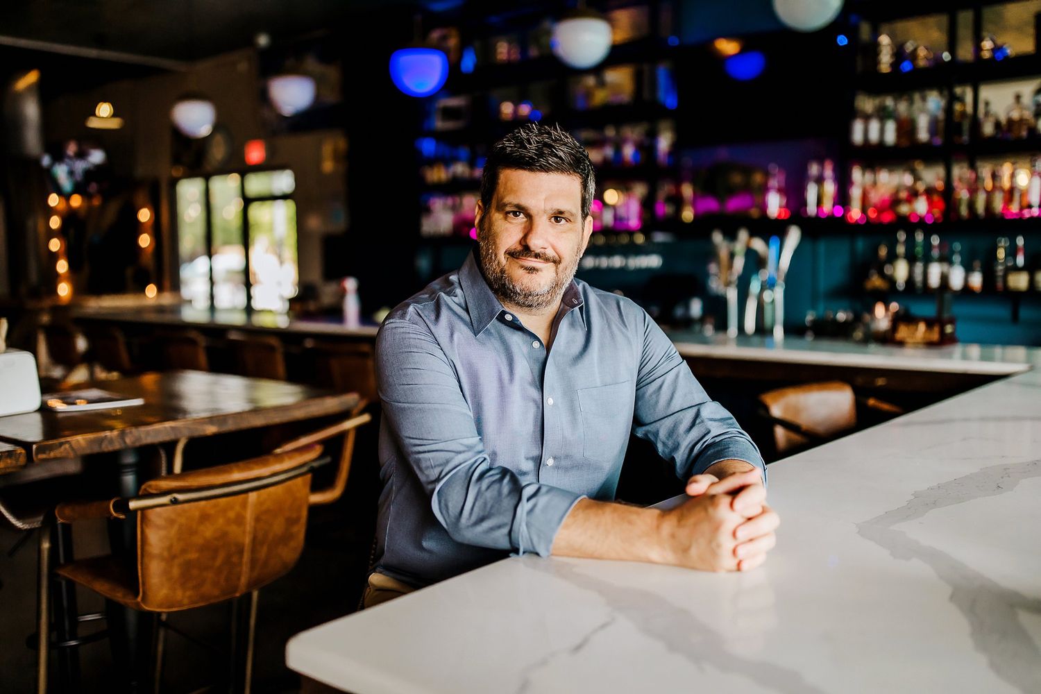 A person sits at a bar counter in a dimly lit restaurant setting with colorful lights in the background.