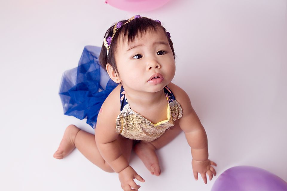 Baby in gold outfit lying on floor during birthday themed photoshoot.