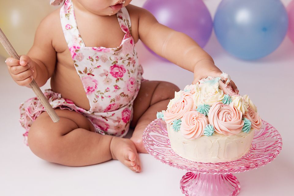 Pink cake smash photography session with floral outfit and pastel decorations.