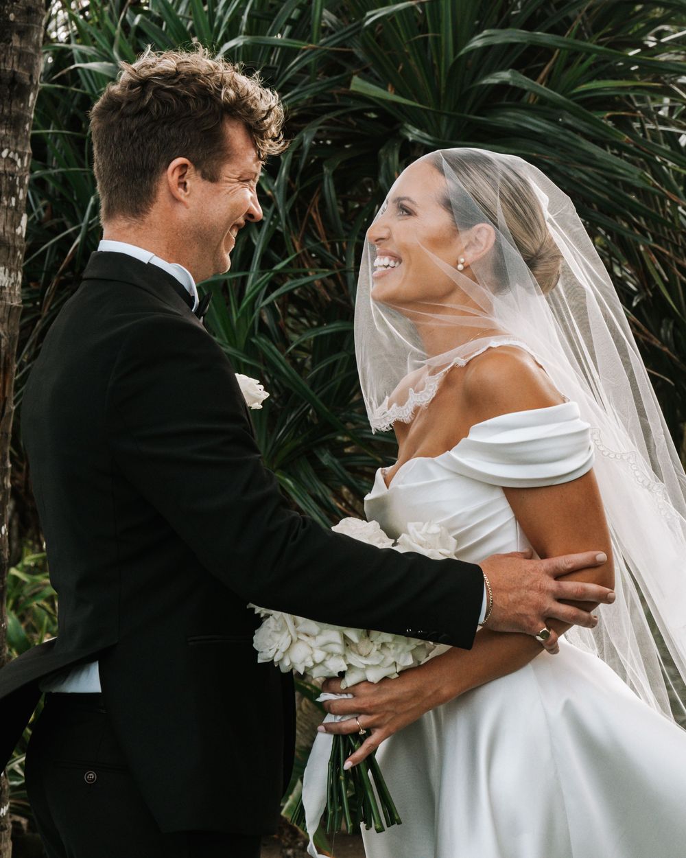 A romantic moment captured between newlyweds on a tropical beach with palm trees in the background.
