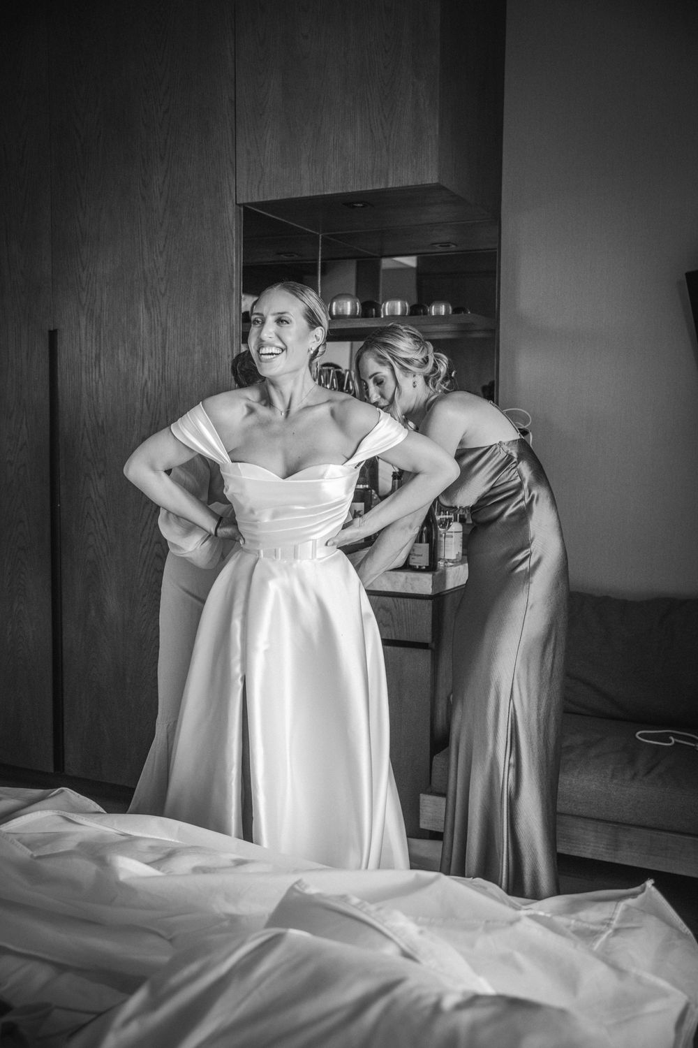 A black and white photo shows final adjustments being made to a wedding dress during preparation moments.