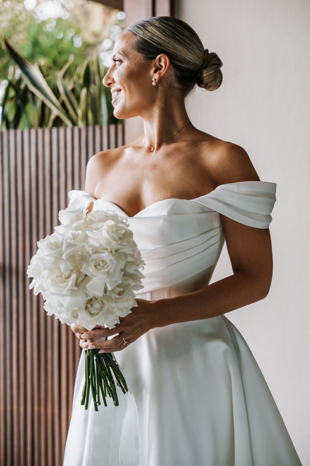 Elegant white bridal bouquet of roses and orchids held against an off-shoulder wedding gown.