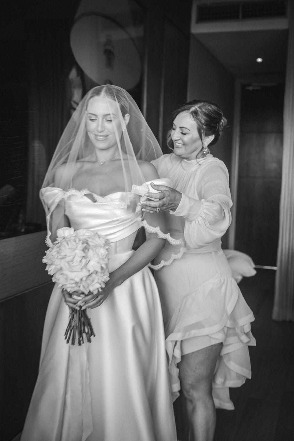 Black and white photos show a bride in a wedding gown getting final adjustments and details before her ceremony.