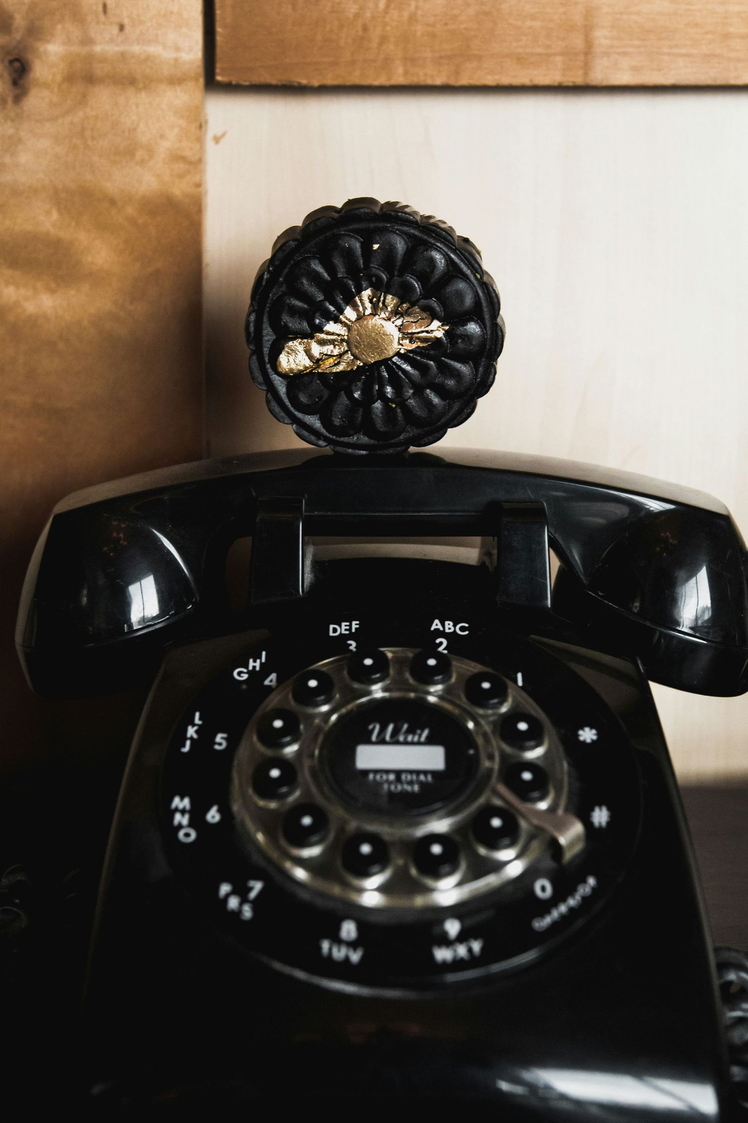 Téléphone rotatif noir vintage avec bouton décoratif, posé sur une surface en bois.