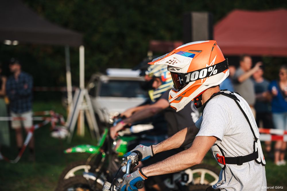 Motocross riders racing on dirt track wearing orange and white gear during competitive event.
