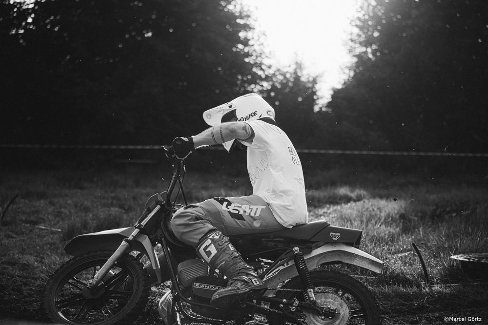 Black and white photo of a vintage motorcycle parked in a grassy field at dusk.