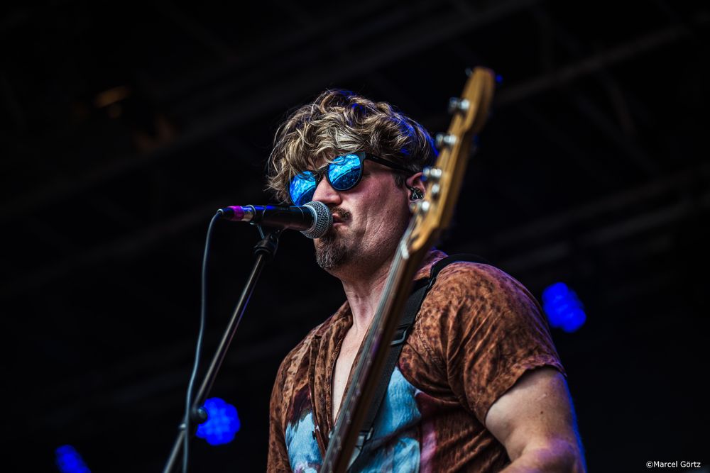 Performer on stage singing passionately into microphone with blue stage lighting in background during live concert performance.