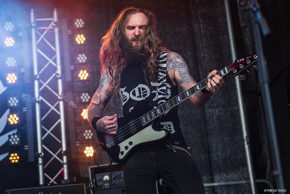 Heavy metal guitarist performs on stage with long hair and tattoos under dramatic concert lighting.