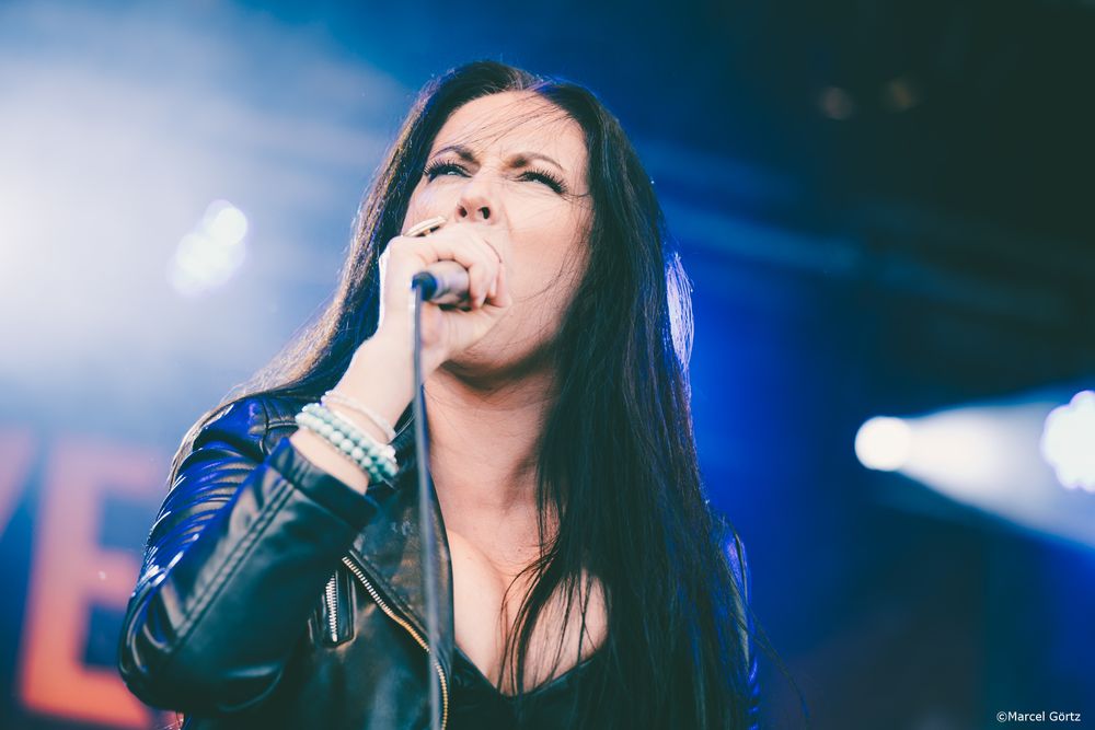 A singer performs on stage with dramatic blue lighting and dark hair in a series of similar concert photos.