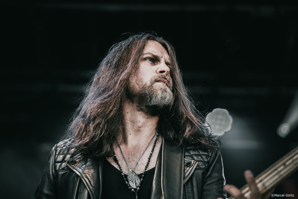 Heavy metal band members perform on stage with dramatic lighting and long hair during a live concert performance.