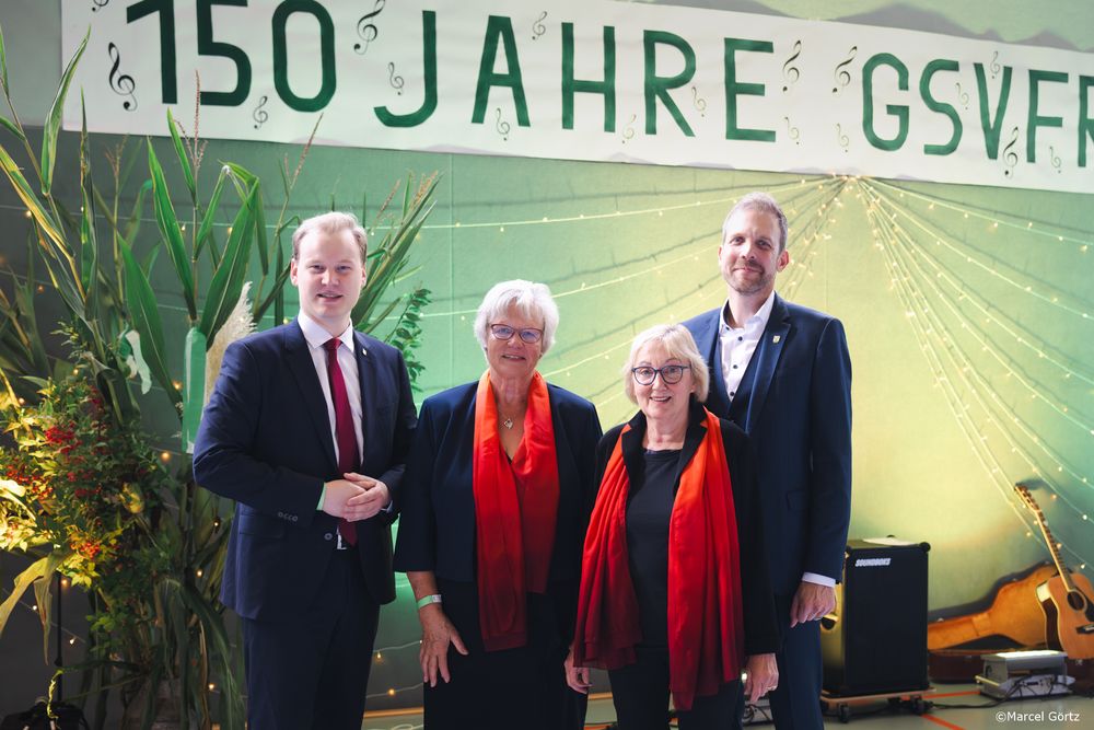 Four people stand in front of a green banner celebrating 150 Jahre GSVFR at an event.