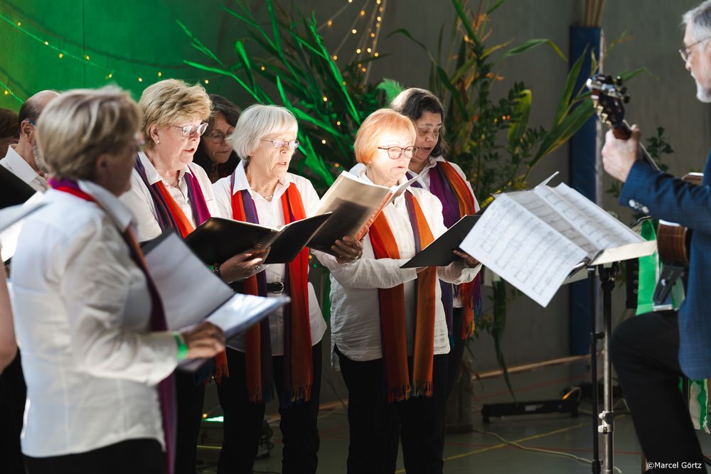 Choir members in formal attire perform together under decorative string lights at an indoor venue.