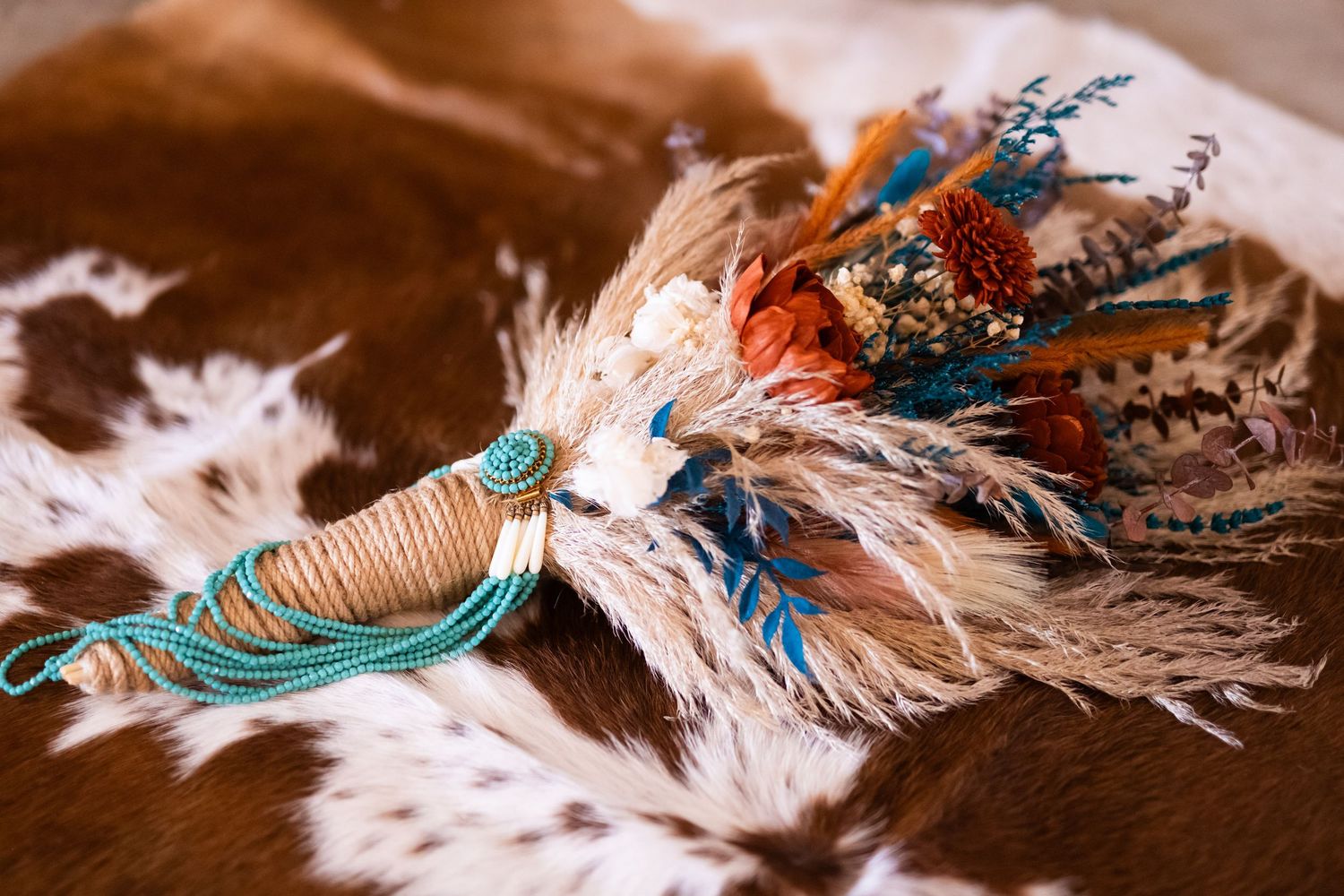 Decorative turquoise and brown western-style tack with feather accents laid out on cowhide.