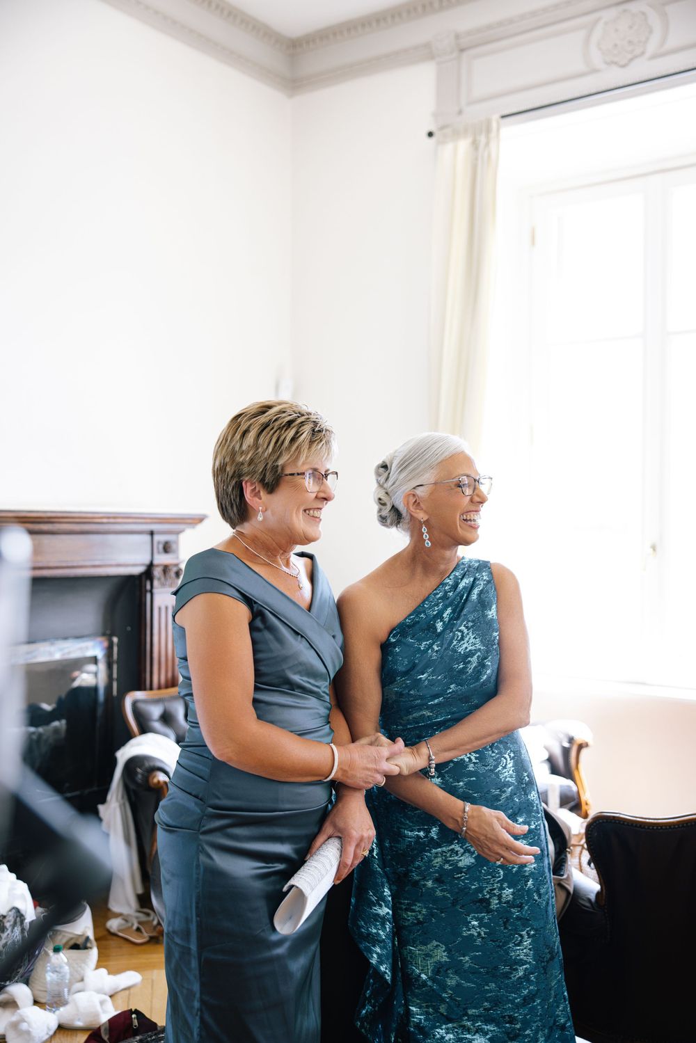 Two women in blue dresses share an emotional moment during wedding preparations.