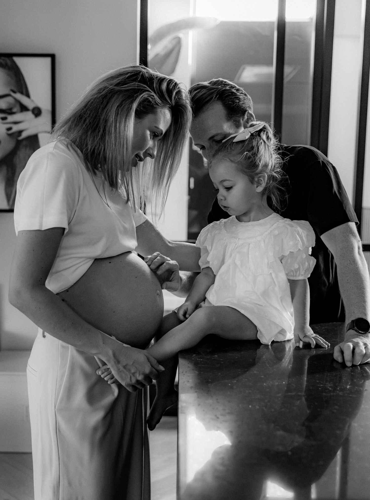 A black and white photo showing a touching moment between expectant parents and child.