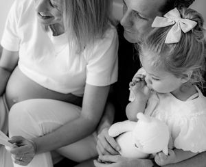 Black and white photo of family moment with child holding stuffed bear.