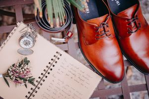 A vintage pocket watch and floral notebook beside polished brown leather dress shoes on brick tiles.
Egy vintage zsebóra és egy jegyzetfüzet