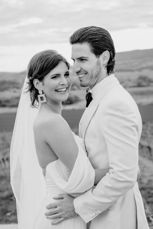 A black and white wedding photo of a happy couple embracing outdoors, with the bride in white and groom in light suit.