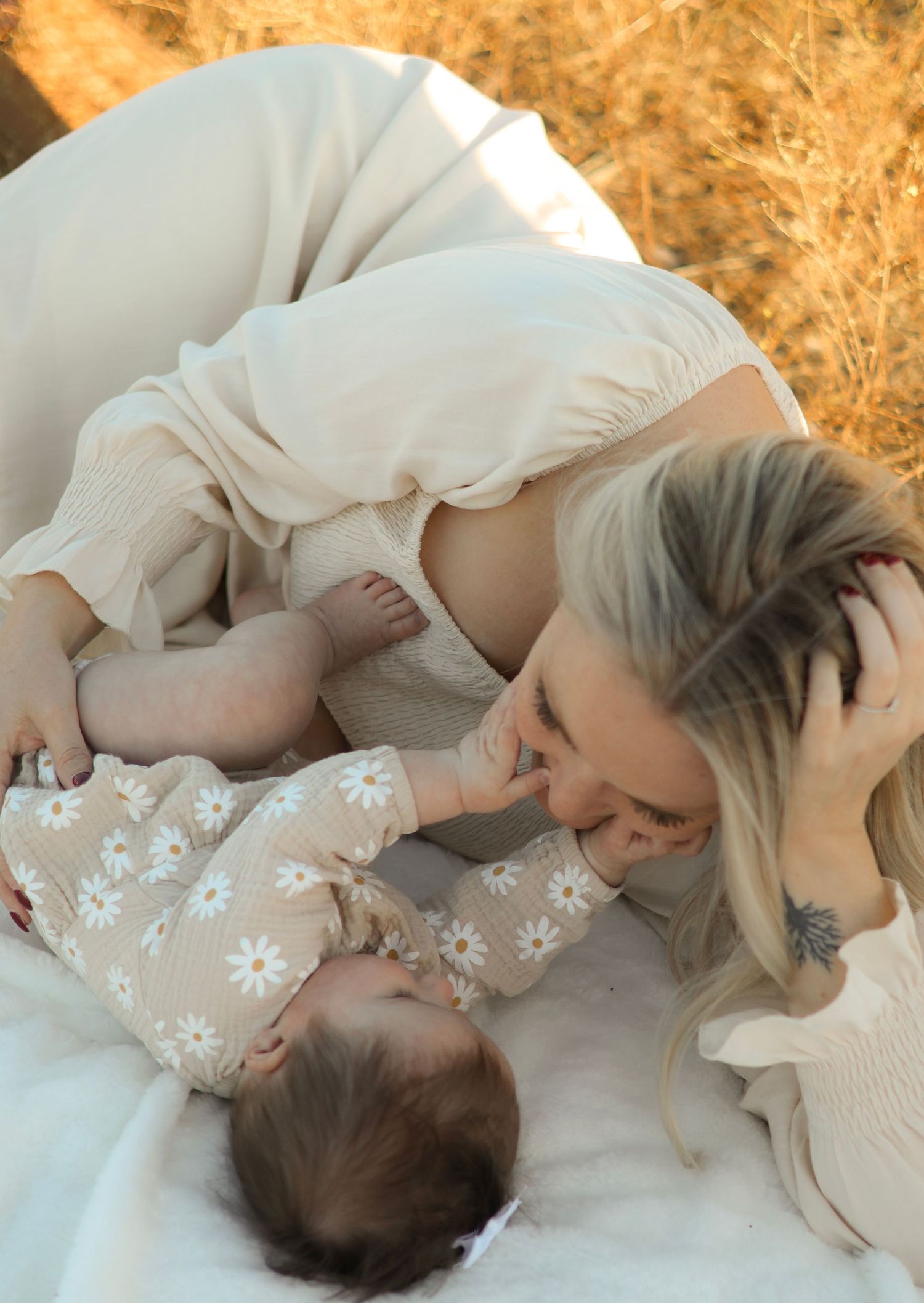 A tender moment between parent and baby laying on white blankets against a golden autumn background in natural light.