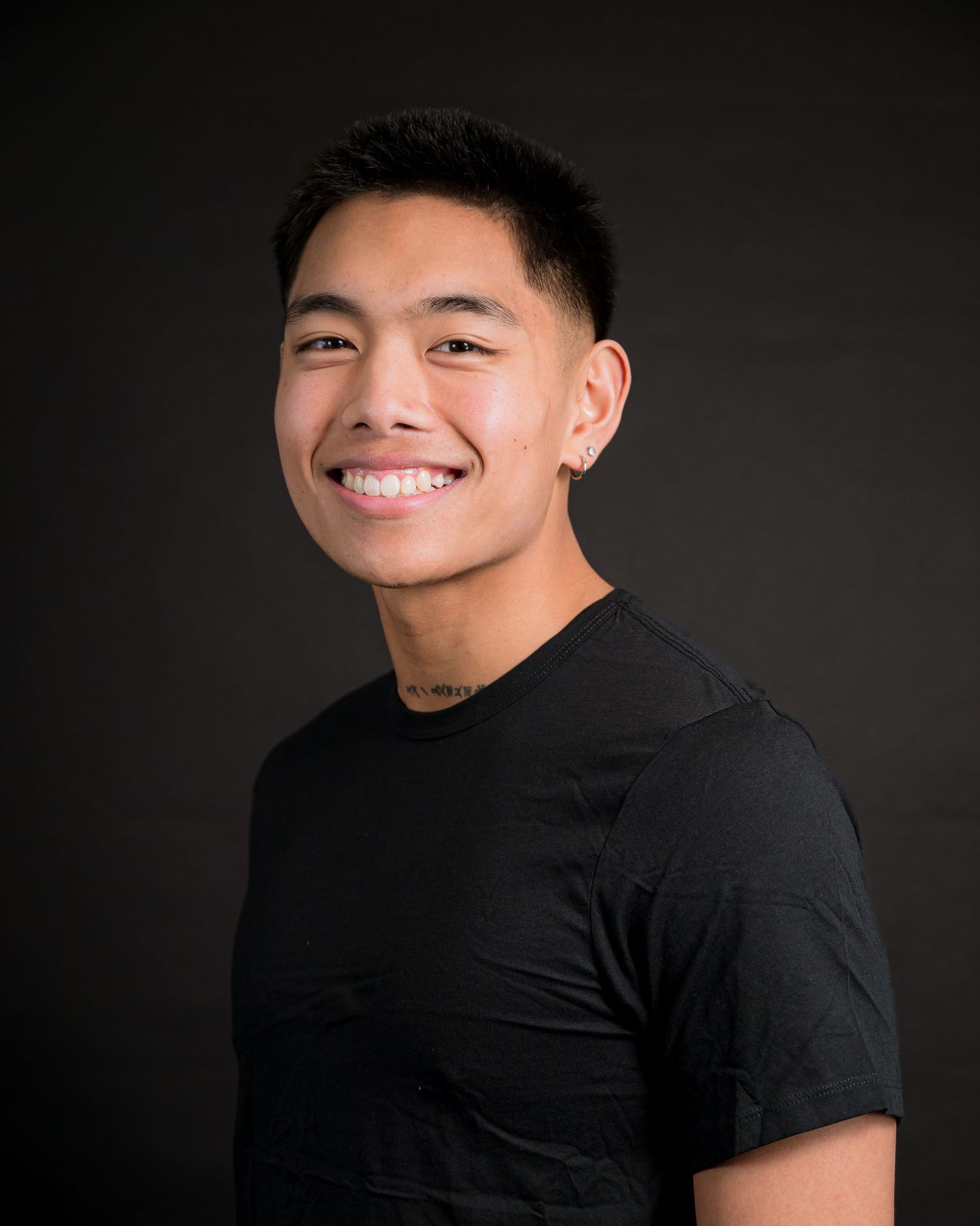 Professional studio portrait against dark background wearing black t-shirt.