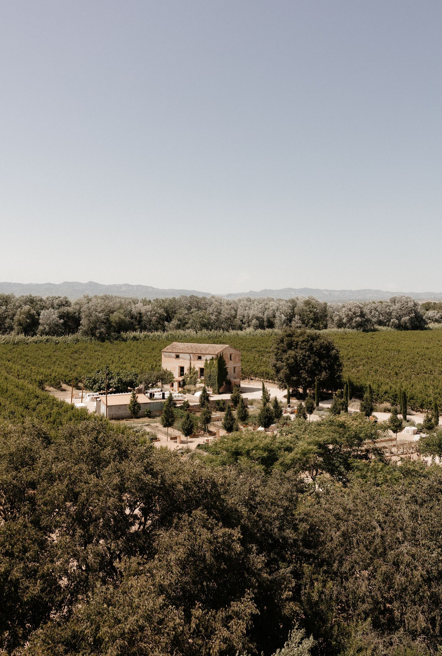 Aerial view of a rustic villa nestled among rolling hills and lush Mediterranean countryside in golden afternoon light.
