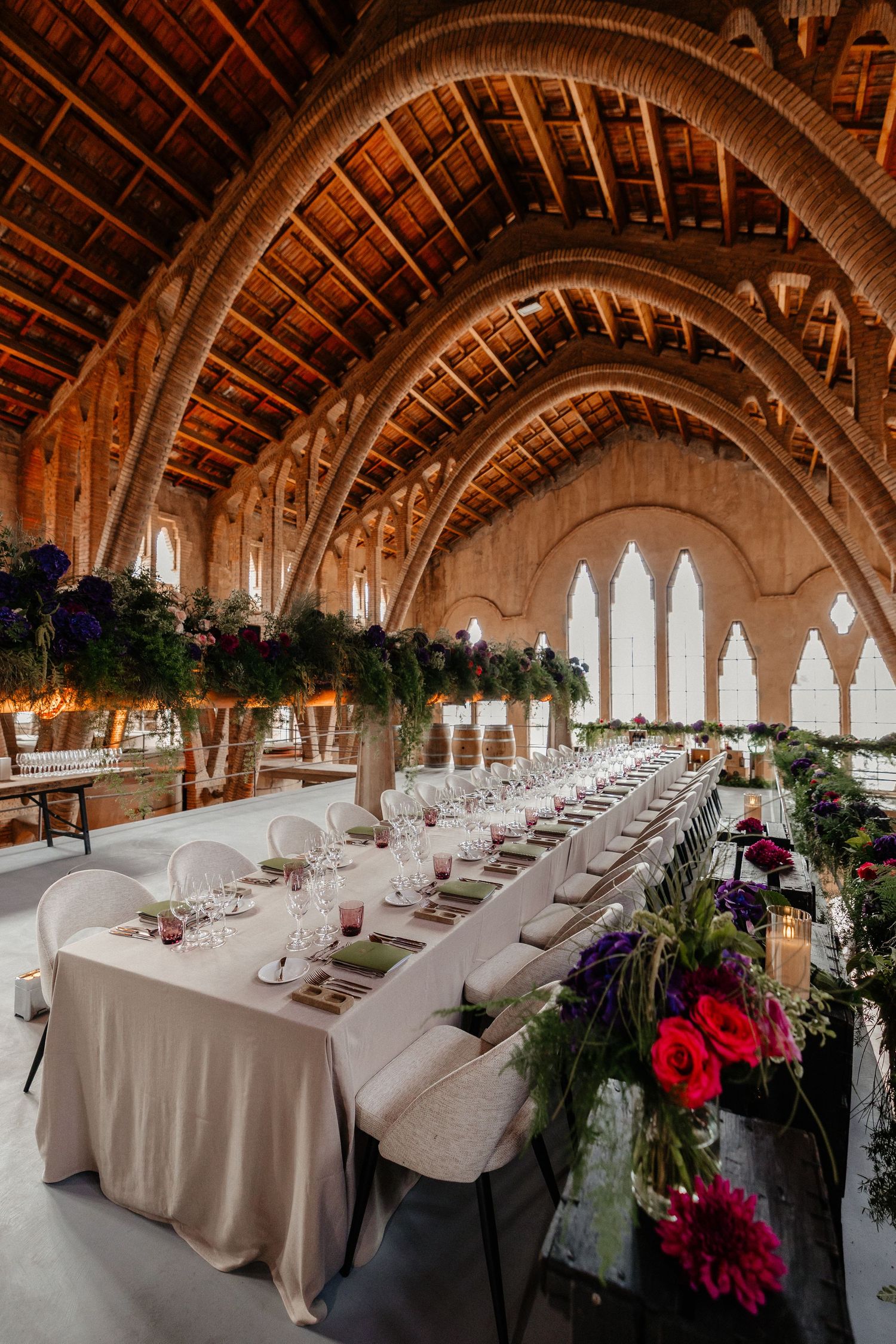 Elegant wedding reception setup in a grand Gothic-style hall with vaulted wooden ceilings and floral table decorations.