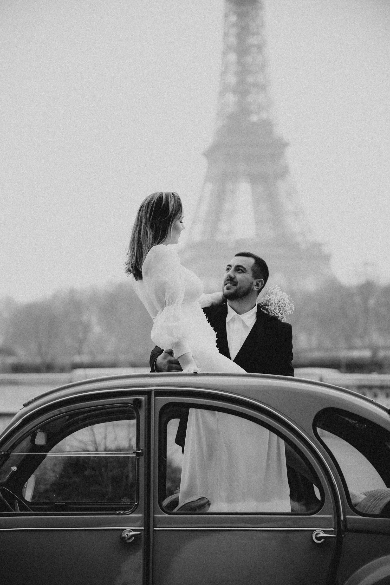 A romantic black and white wedding photo with a vintage car and the Eiffel Tower in Paris.